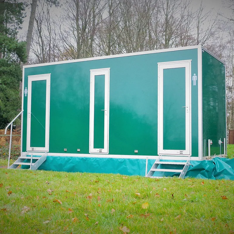 A green luxury toilet trailer standing level on firm grass, with steps up to each door