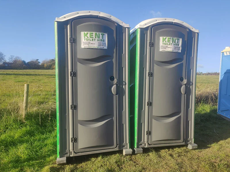 Two of our Kent Toilet Hire portable toilets standing side by side in a field