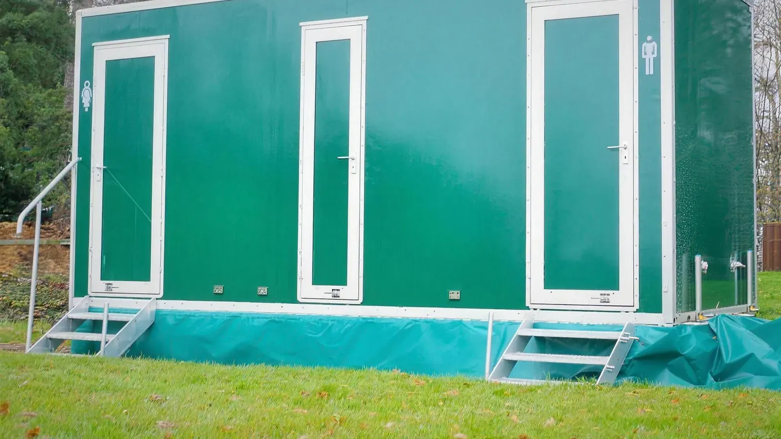 One of our green luxury toilet trailers set up on a lawn in front of trees
