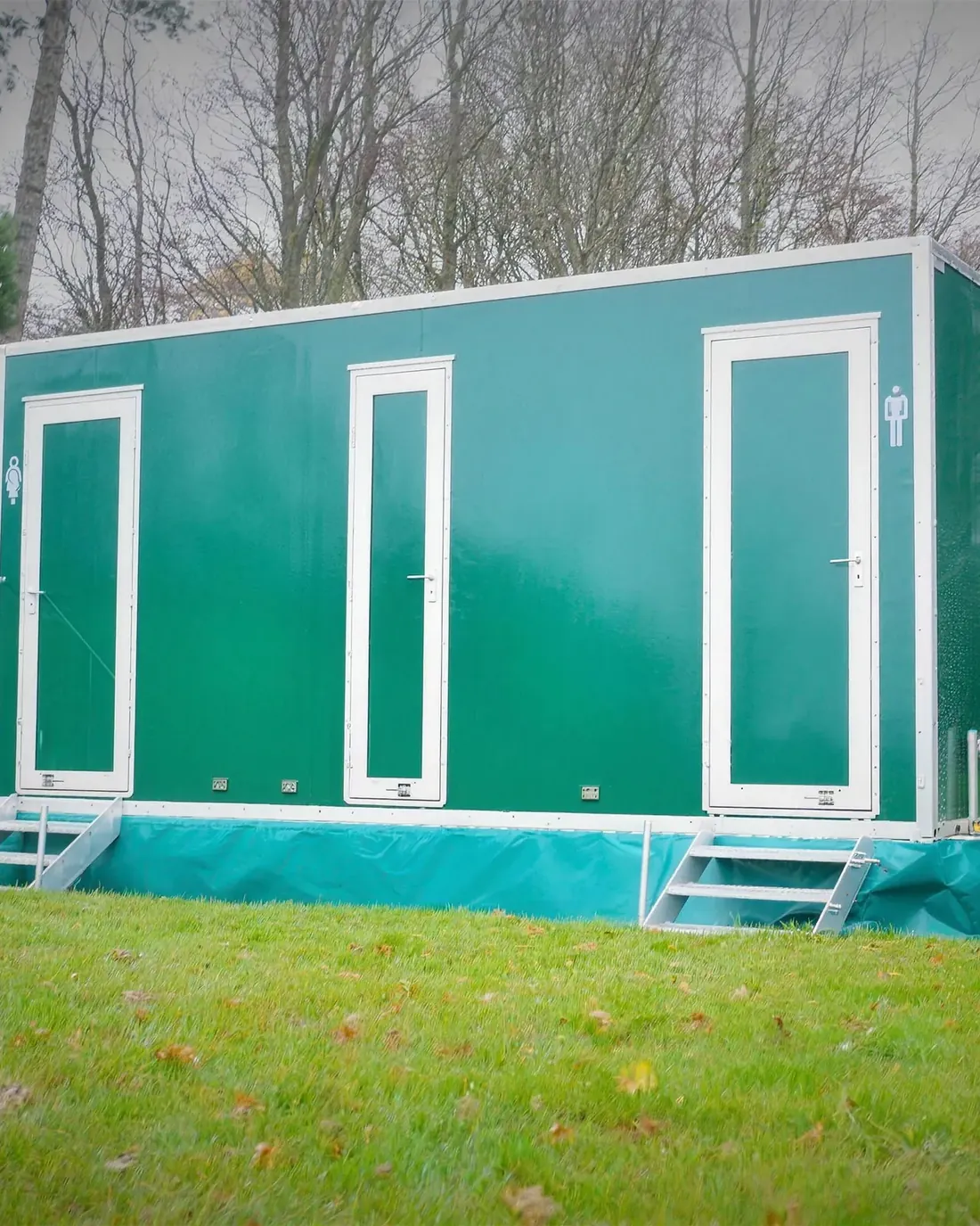 One of our green luxury toilet trailers on a lawn, with steps up to the ladies and gents doors