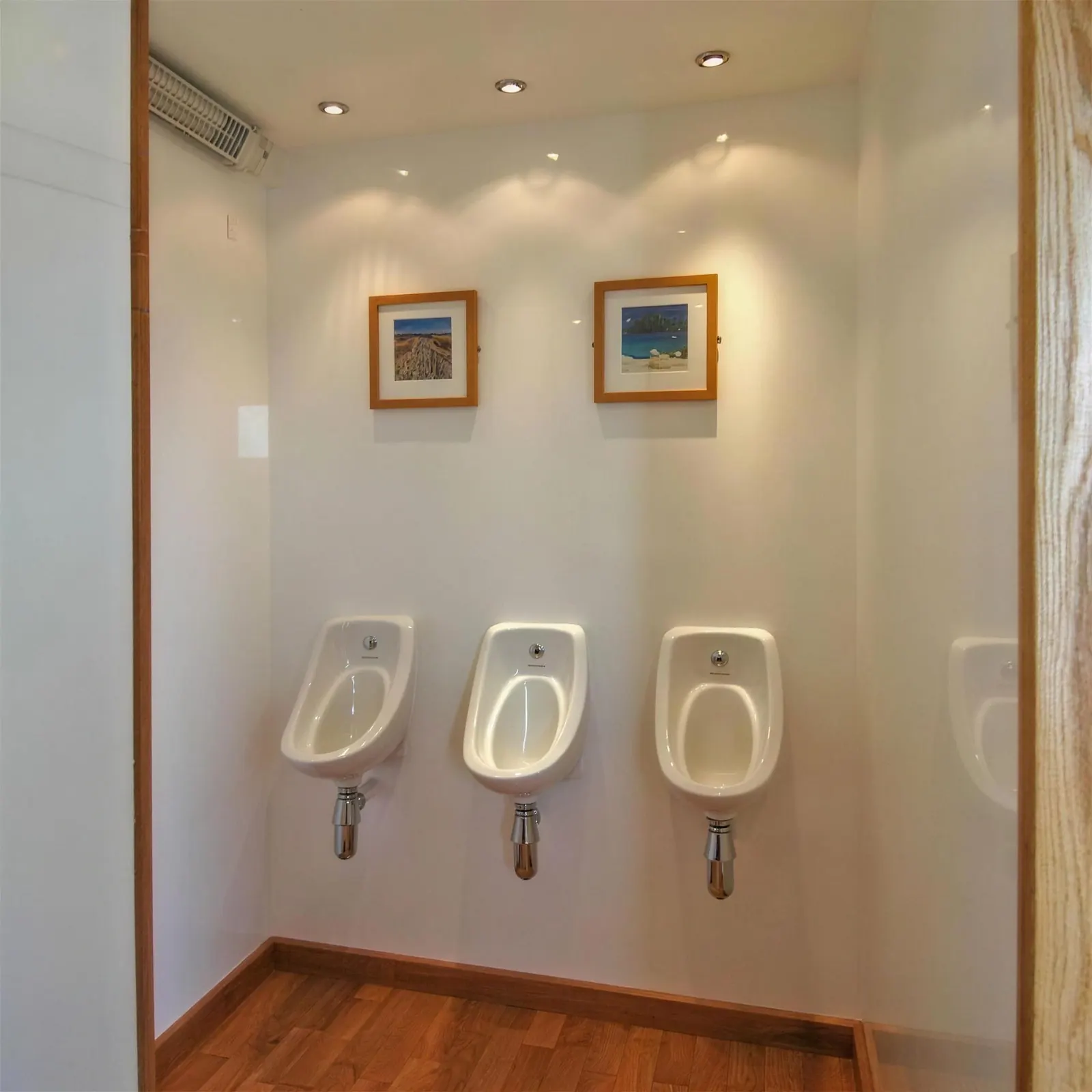 The gents' side of a luxury trailer with three urinals and framed prints