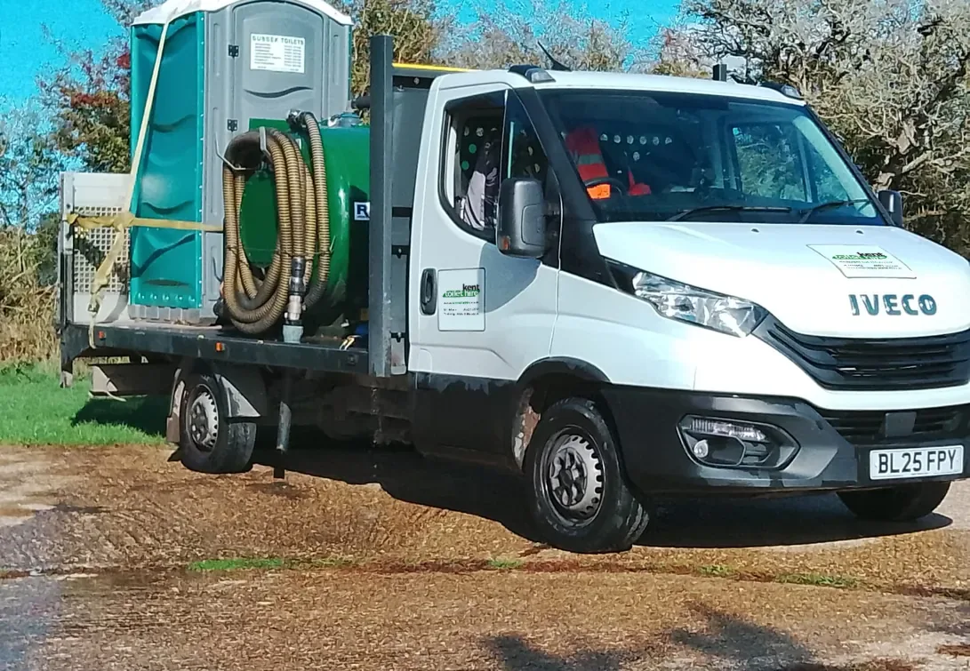 Our white pump truck with a portable toilet, a waste tank and its hose reel on the back, parked on gravel